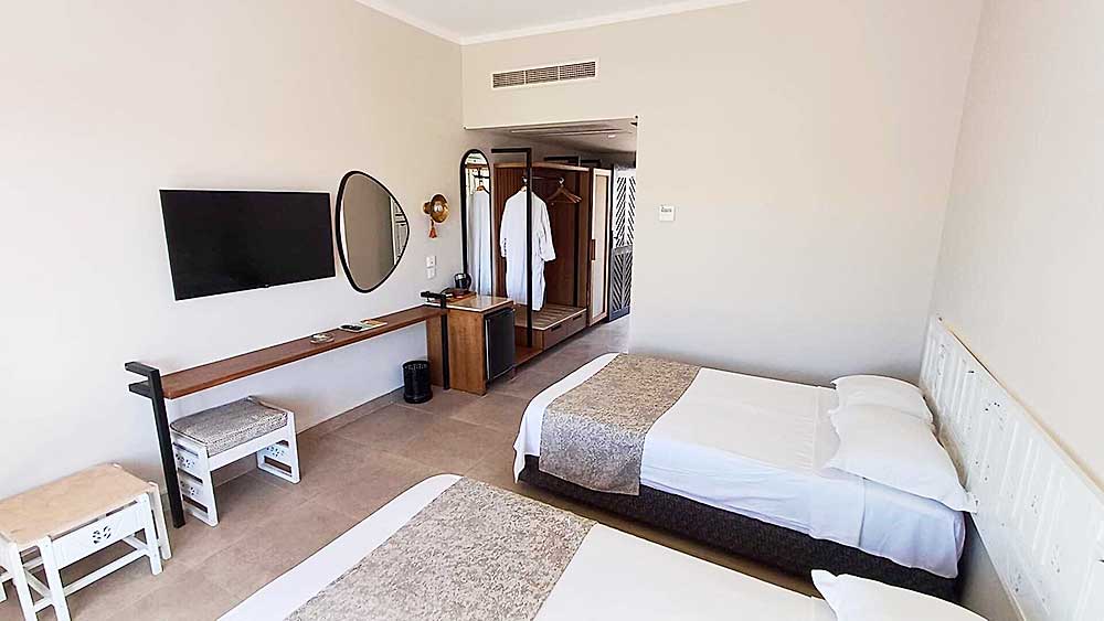 Una camera d'hotel ordinata e moderna nel Villaggio Sharm El Sheikh dotata di letti gemelli, TV a schermo piatto e armadio aperto.