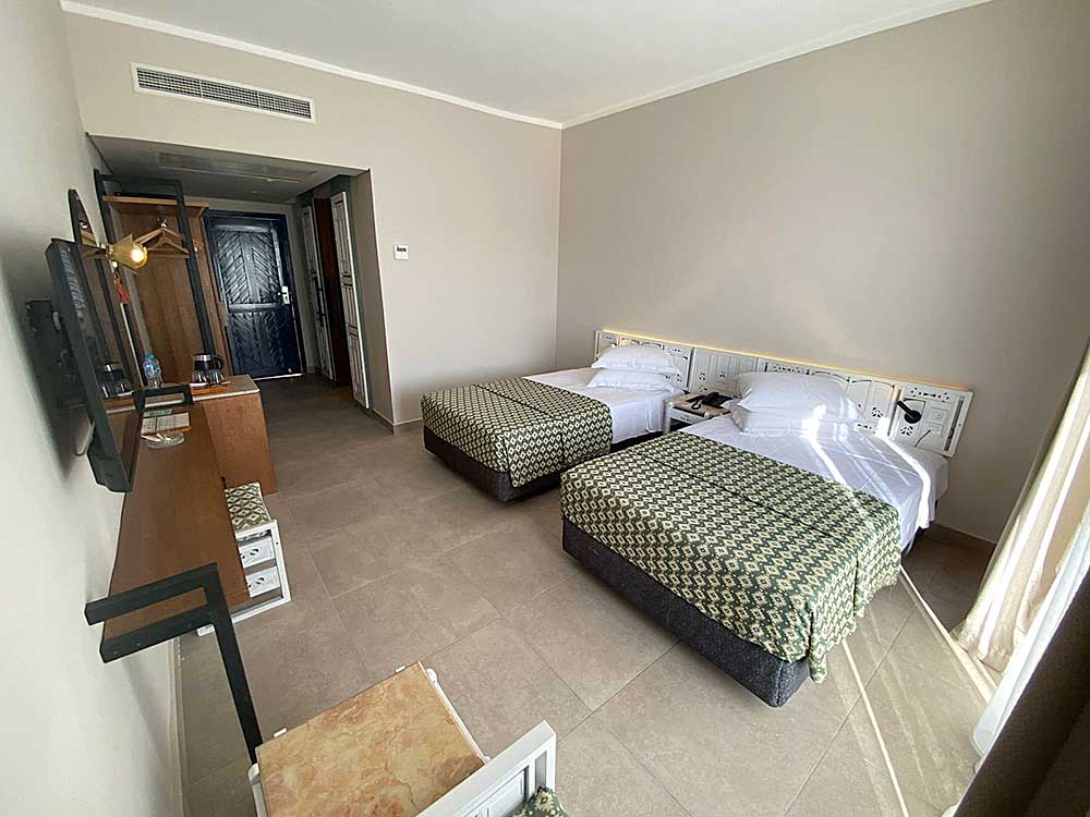 Camera d'hotel con due letti gemelli, TV e porta aperta su un'altra stanza al Villaggio Sharm El Sheikh.