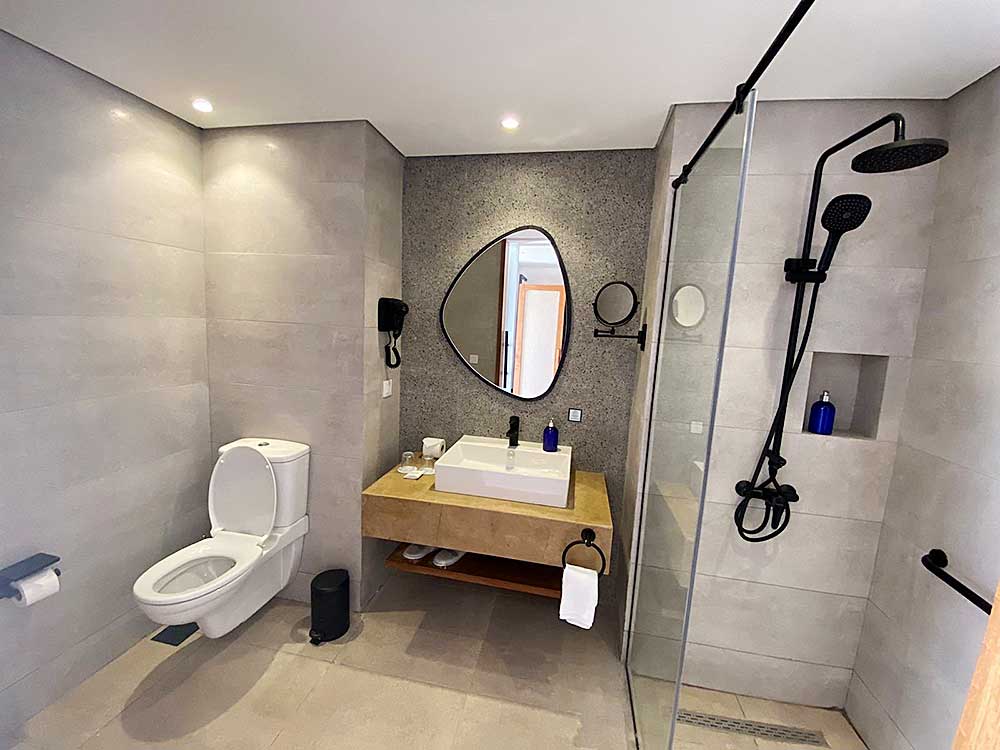 Interno del bagno moderno con cabina doccia, WC a parete e lavandino sotto uno specchio ovale al Villaggio Sharm El Sheikh.