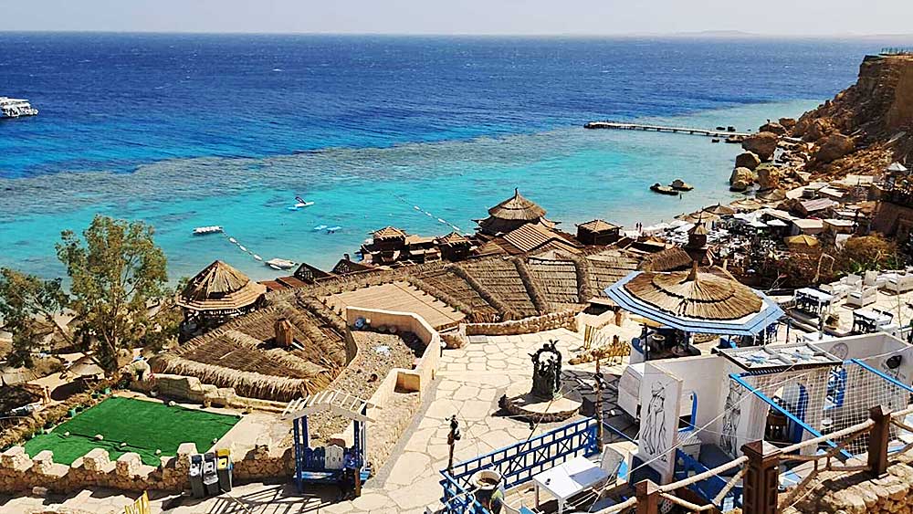 Una località costiera con strutture dal tetto di paglia che si affaccia su un mare cristallino con barche nel villaggio di Sharm El Sheikh.