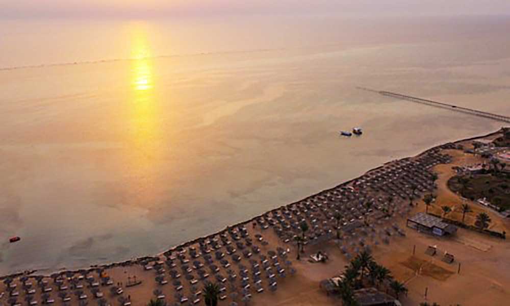 Alba su una tranquilla spiaggia fiancheggiata da ombrelloni di paglia e un mare calmo nell'offerta villaggio Marsa Alam.