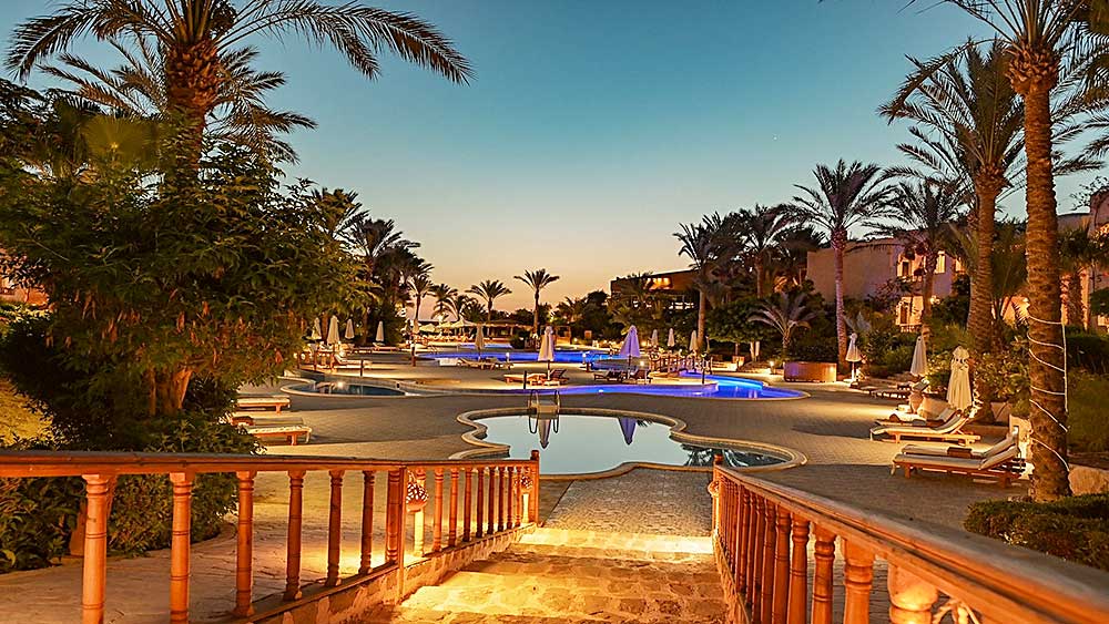 Vista crepuscolare della piscina del Resort Villaggio Mar Rosso circondata da palme e illuminata da luci calde.