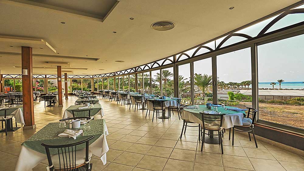 Ampio ristorante sulla spiaggia interno con tavoli ben disposti e ampie vetrate con vista sul mare, parte dell'offerta Villaggio Mar Rosso.