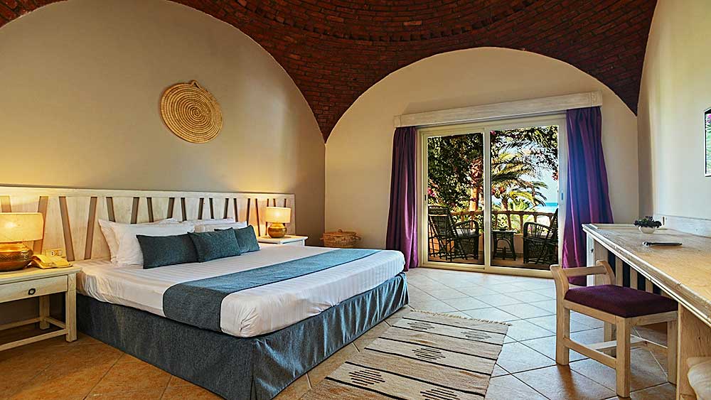 Camera d'albergo spaziosa e luminosa al Villaggio Mar Rosso con ingresso ad arco su un balcone con vista sul verde.