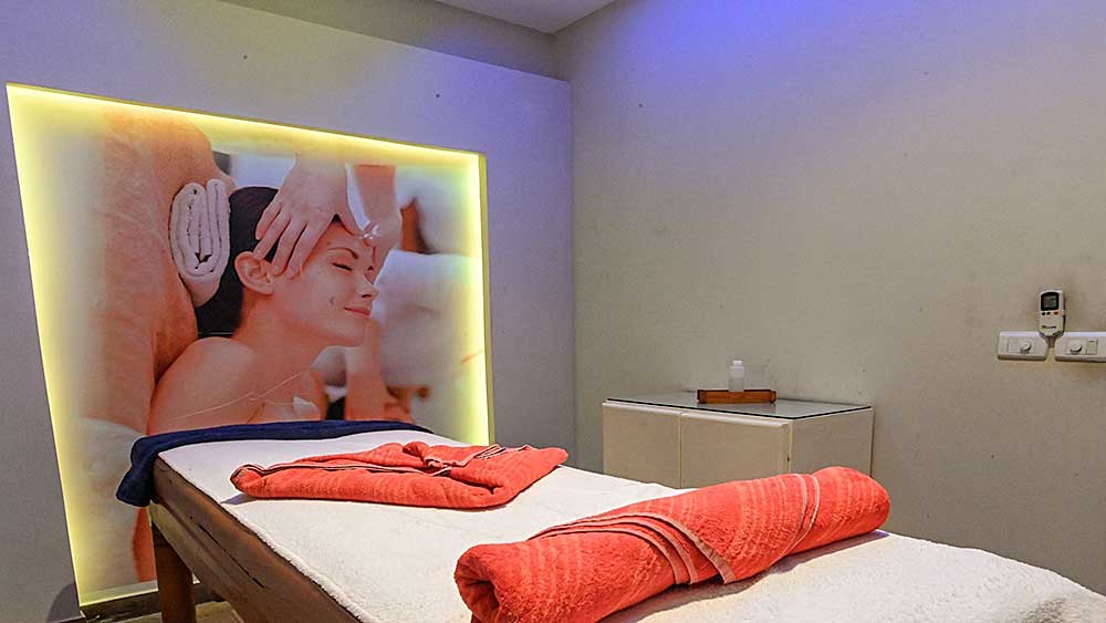Una sala massaggi con lettino e asciugamani ben preparati nel Villaggio Mar Rosso, con l'immagine in controluce di una persona che riceve un trattamento viso.