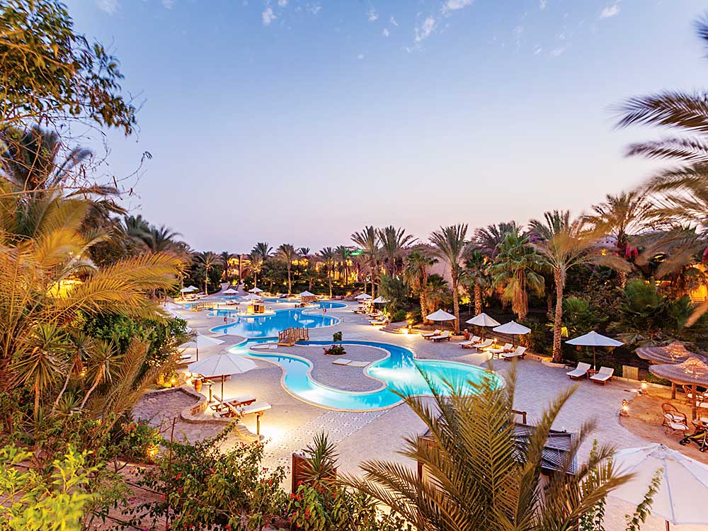 Un'ampia piscina all'aperto circondata da palme e lettini durante il crepuscolo al Villaggio Mar Rosso.