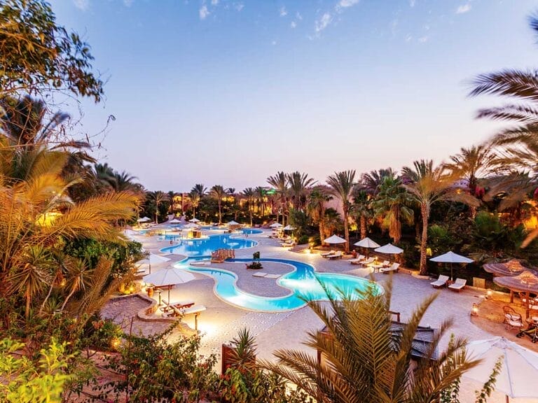 Piscina del resort tropicale circondata da palme durante il crepuscolo al Villaggio Marsa Alam.