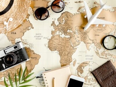 Mappa del mondo, modello di aereo, macchina fotografica, occhiali da sole, cappello, passaporto, taccuino e smartphone su una scrivania.