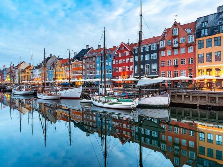 Edifici colorati fiancheggiano il lungomare di Nyhavn a Copenaghen, in Danimarca, una delle incantevoli capitali scandinave, con diverse barche a vela ormeggiate e un calmo riflesso d'acqua perfetto per i viaggi europei.