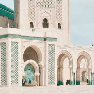 Un edificio grandioso e decorato con ingressi ad arco e intricate piastrelle verdi e bianche. Diverse persone sono visibili vicino agli archi, vivendo il fascino di questa meraviglia architettonica. Scopri questi luoghi incantevoli con l'offerta viaggio in Marocco di SBS Viaggi.