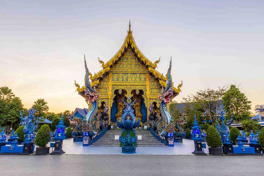 Vista frontale del Wat Rong Seur Ten, conosciuto anche come il Tempio Blu, a Chiang Rai, Thailandia. Il tempio presenta disegni decorati in oro e blu con statue di draghi all'ingresso. Scopri questa meraviglia con l'esclusiva offerta viaggio in Thailandia di SBS Viaggi!