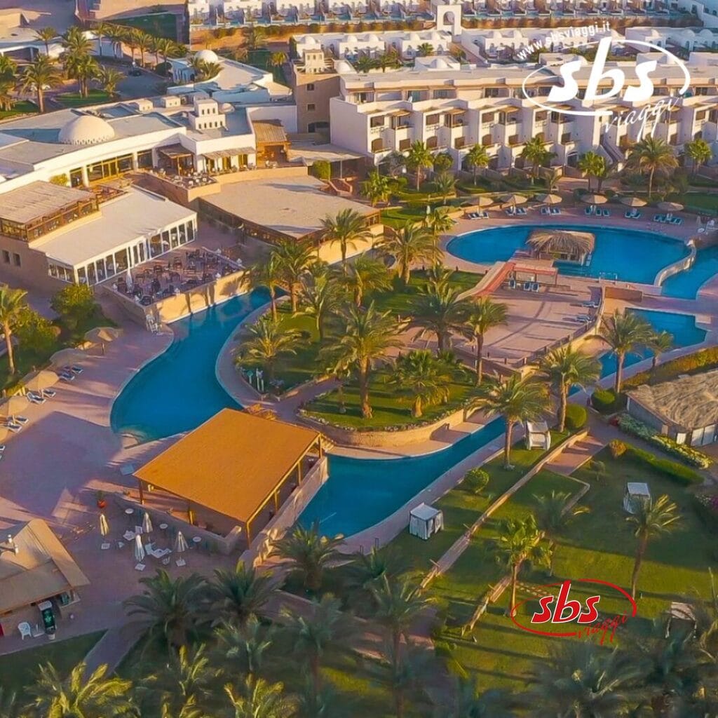 Vista aerea del Fort Arabesque Resort con numerose piscine, ville, palme, edifici circostanti e aree lounge in un ambiente soleggiato.