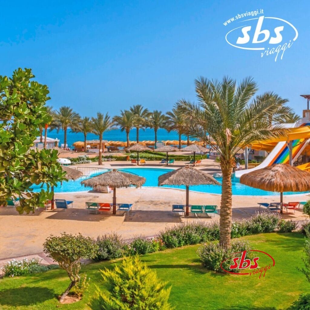 Un resort tropicale con palme, una grande piscina, diversi ombrelloni di paglia, sedie a sdraio, scivoli d'acqua e un cielo azzurro e limpido sullo sfondo. Scopri il fascino di Soma Bay al Caribbean World Resort. Il logo del sito web 