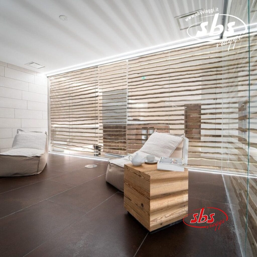 Moderna area lounge spa con arredamento minimalista al TH Courmayeur, con comode sedute, elementi in legno e un'atmosfera serena. Le tende a strisce lasciano filtrare la luce per creare un'atmosfera rilassante.