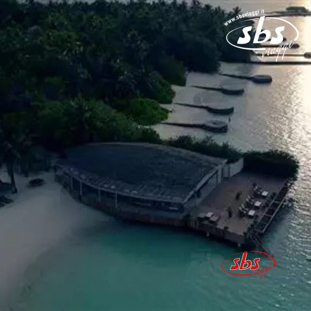 Vista aerea di un ristorante sulla spiaggia del Nika Island Resort, con posti a sedere all'aperto, circondato da alberi e barche attraccate su una spiaggia tranquilla vicino alla spa.