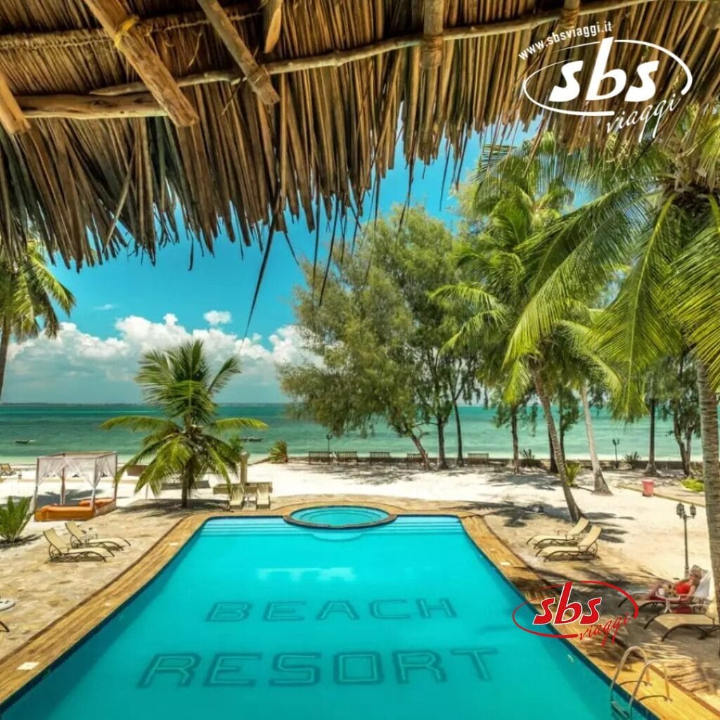 Si apre una vista mozzafiato sul resort tropicale sulla spiaggia del Club Coralia, con una piscina scintillante in primo piano, palme ondeggianti e una spiaggia sabbiosa incontaminata che conduce all'oceano sotto un cielo azzurro e limpido.