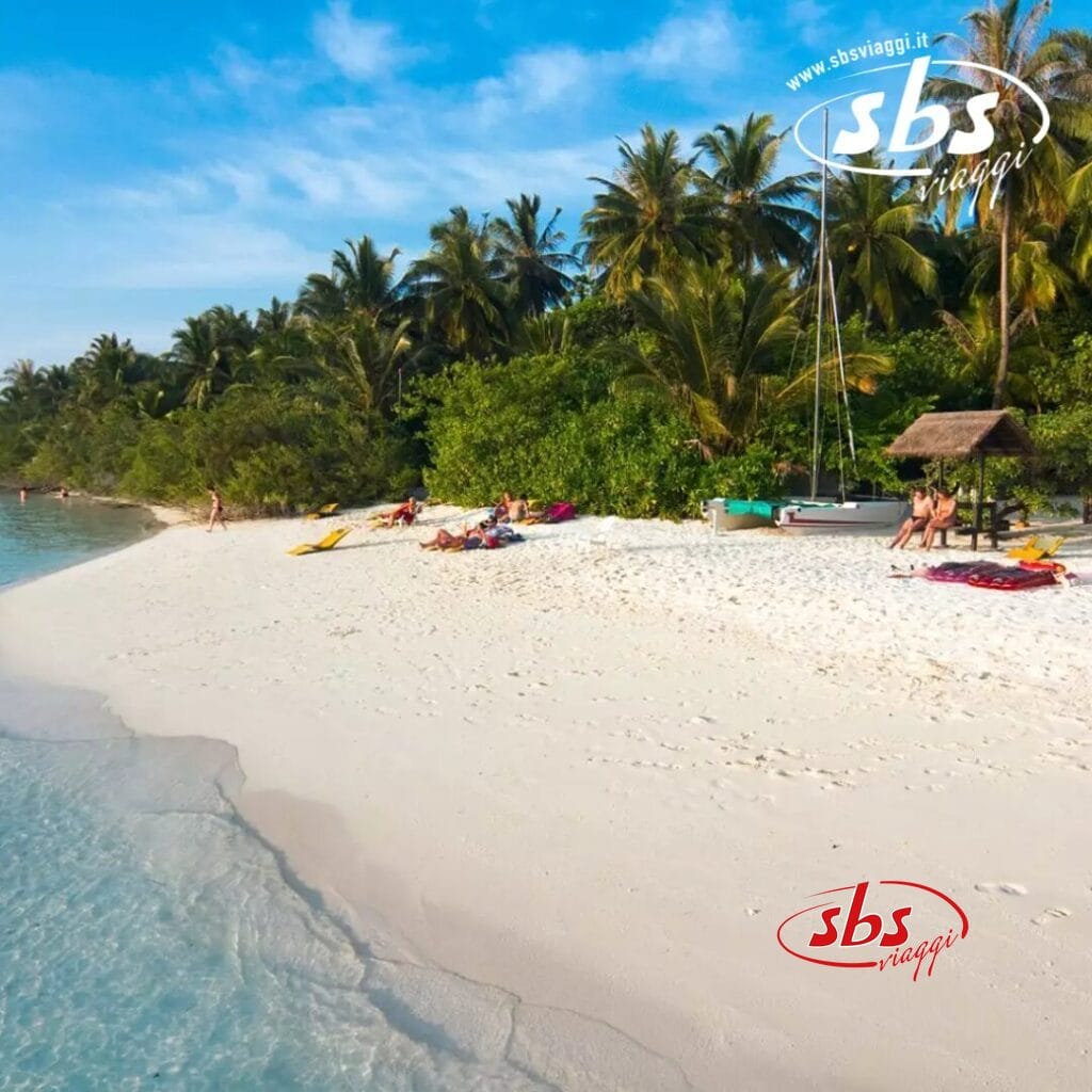 Scena di spiaggia tropicale con persone che si rilassano sulla sabbia bianca dell'isola di Embudu vicino all'acqua limpida, circondate da palme e vegetazione lussureggiante. Una piccola struttura con tetto di paglia, tipica del fascino pittoresco che si trova in un resort sull'isola, è visibile sullo sfondo.