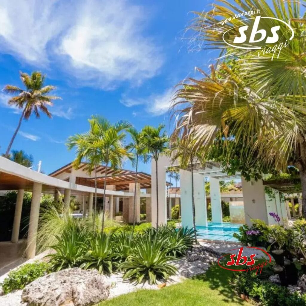 Un lussureggiante giardino tropicale con palme e un cielo azzurro terso circonda un moderno padiglione all'aperto e un'area piscina, creando l'oasi perfetta per un resort sulla spiaggia di Punta Cana. Godetevi l'atmosfera serena arricchita da un'invitante esperienza spa.