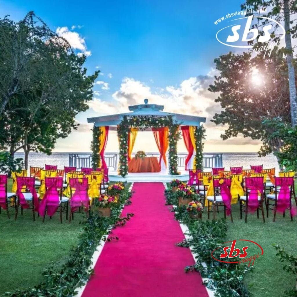 Questa squisita location per matrimoni all'aperto presso l'Hilton La Romana presenta una suggestiva navata rossa, sedie vivaci e un gazebo splendidamente decorato in riva all'oceano. Circondato da alberi sotto un sole splendente, offre un ambiente idilliaco per il tuo giorno speciale.