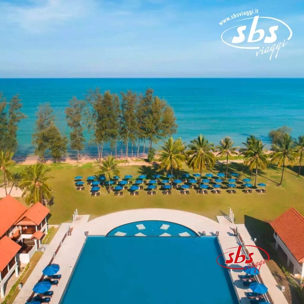 Vista aerea di un resort fronte oceano con una grande piscina, caratterizzata da elementi di design Bozza Automatica, circondata da palme e lettini prendisole, di fronte al mare.