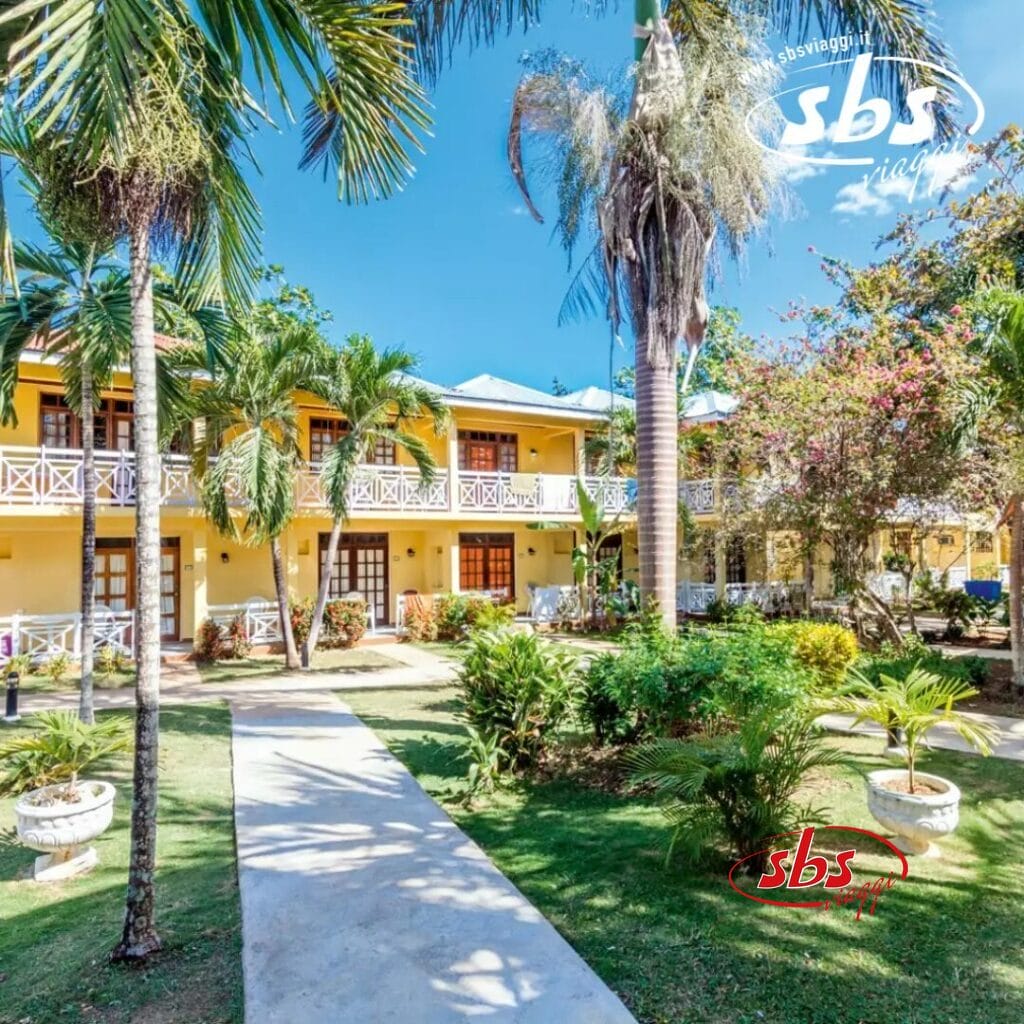 Il Merril's Beach Resort vanta un cortile tropicale adornato da palme, incastonato in un edificio giallo a due piani e sotto un limpido cielo azzurro.