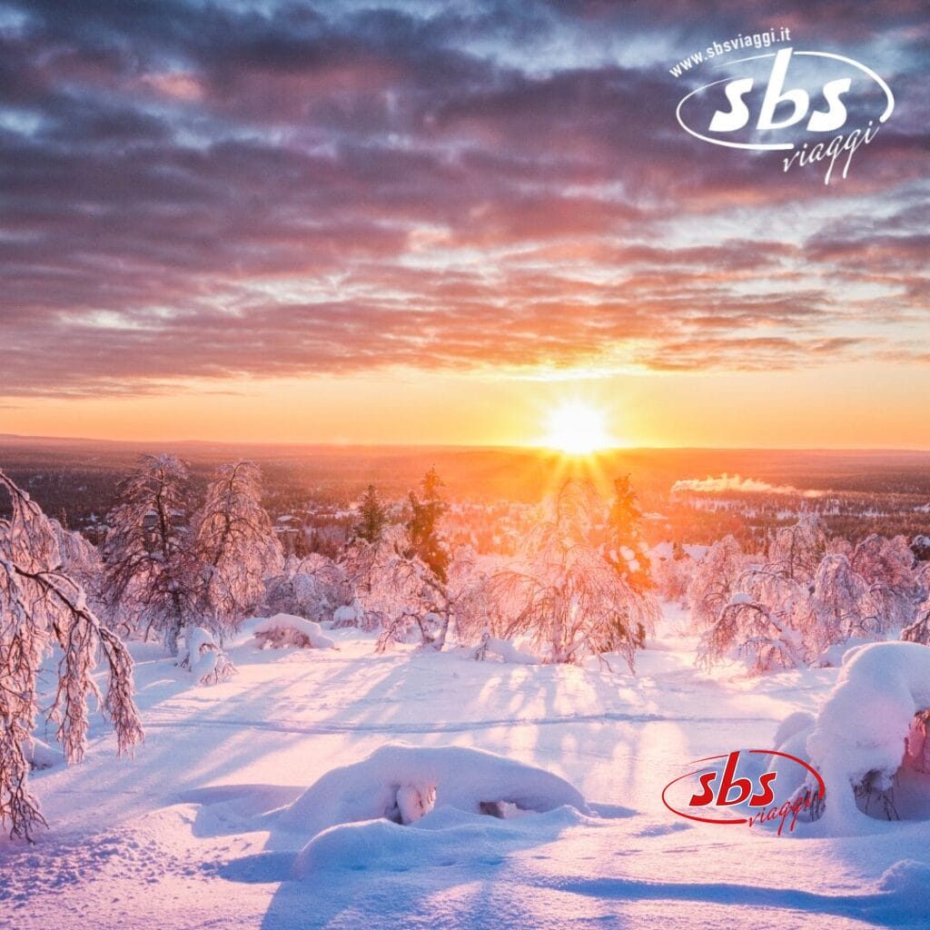 Un paesaggio innevato in Lapponia finlandese presenta alberi spogli al tramonto sotto un cielo parzialmente nuvoloso. La luce del sole proietta lunghe ombre sulla neve incontaminata mentre un lontano husky attraversa silenziosamente la scena. Il logo nell'angolo in alto a destra recita 