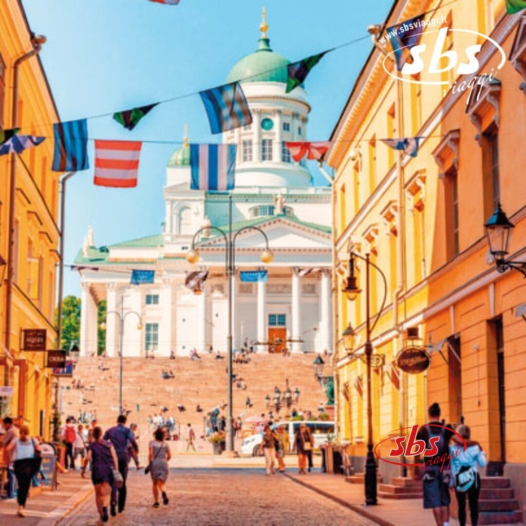 Vista sulla strada che conduce all'iconica Cattedrale di Helsinki, brulicante di gente che passeggia e di bandiere colorate che danzano sopra: una tappa perfetta della tua crociera sul Baltico.