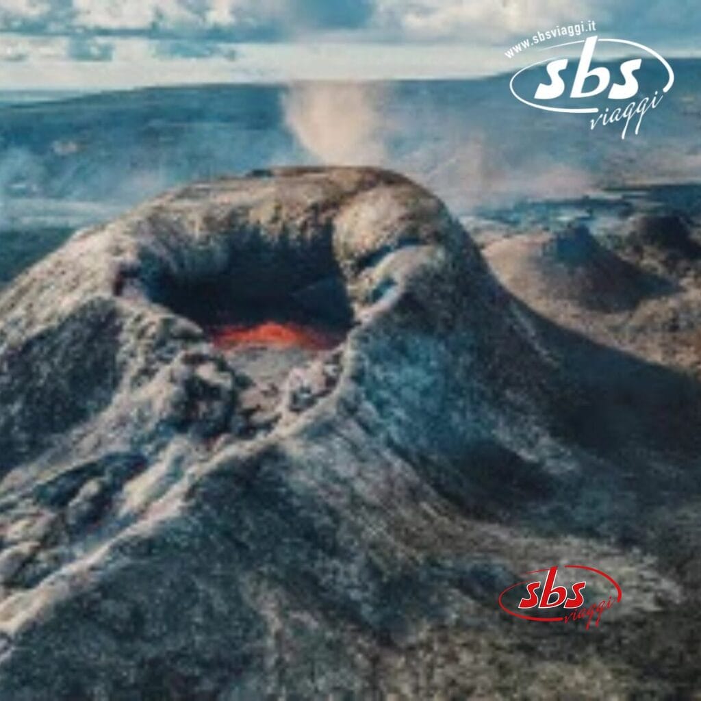 Vista aerea di un vulcano attivo con il fumo che sale dal suo cratere, circondato da un terreno accidentato, che crea uno sfondo spettacolare che invita l'immaginazione a rilassarsi e a vagare, come se si esplorasse un paesaggio surreale, magari visto durante il Capodanno in Islanda.