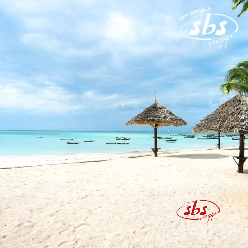 La scena della spiaggia tropicale è caratterizzata da sabbia bianca e acqua turchese sotto un cielo nuvoloso, con barche di legno che ondeggiano dolcemente. Nelle vicinanze, due ombrelloni di paglia offrono ombra a coloro che assaporano il perfetto mix di bellezza naturale e bozza automatica.