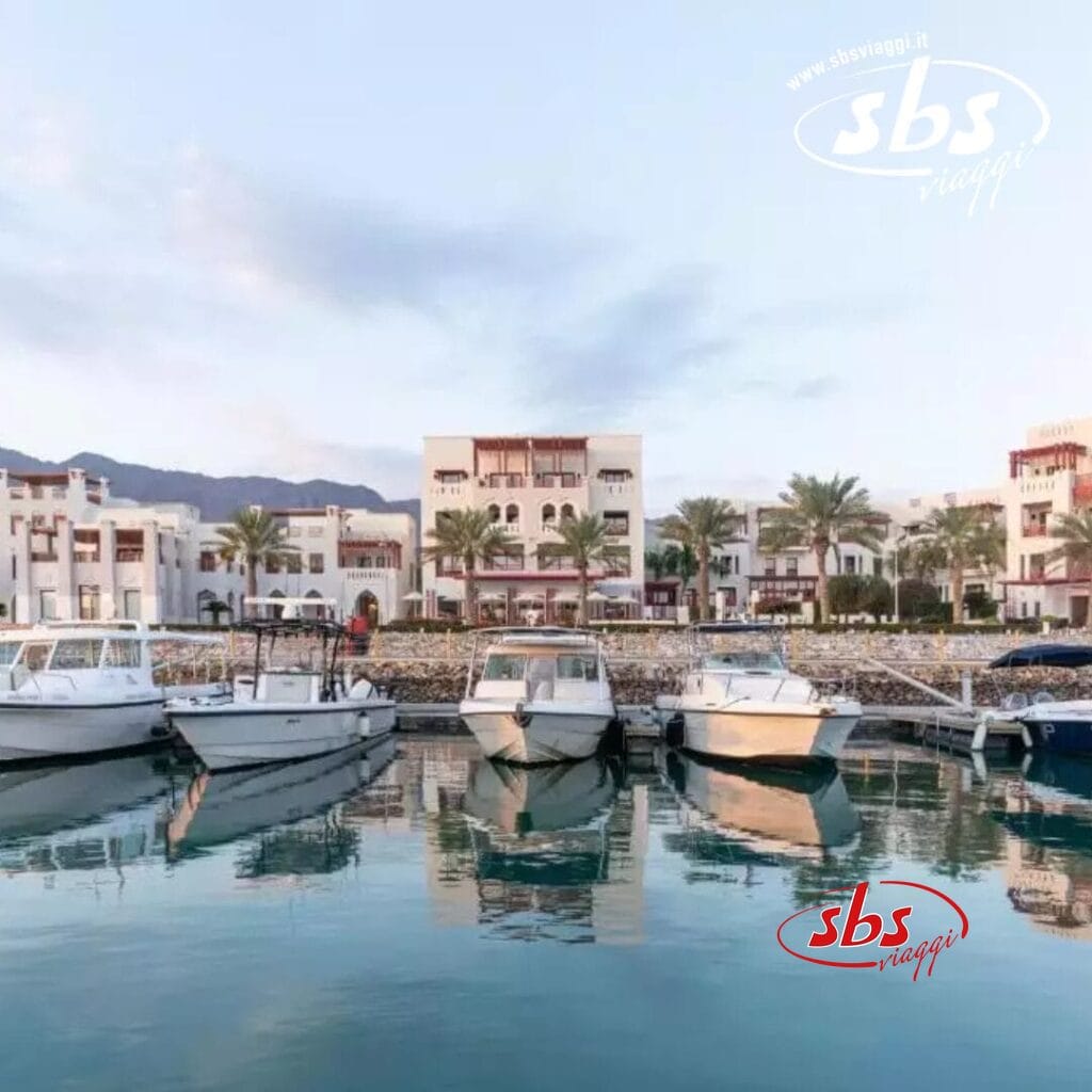 Le barche attraccano in un tranquillo porto turistico di fronte al Sifawy Boutique Hotel, con le palme che ondeggiano dolcemente e le montagne che si stagliano contro il cielo limpido sopra di loro.