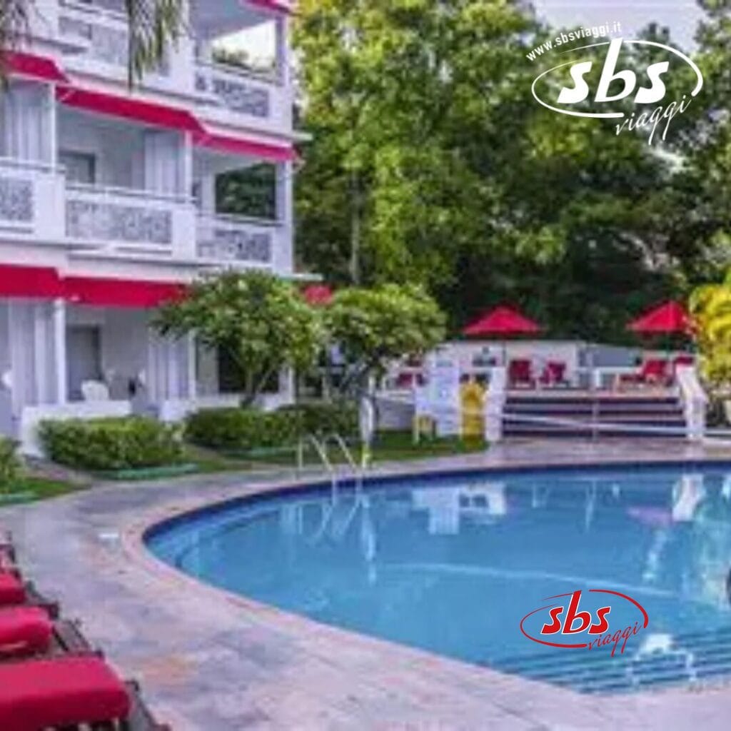 Vista sulla piscina dell'hotel Royal Decameron Montego Beach con elementi di design rossi e bianchi, circondato da una vegetazione lussureggiante e sedie a sdraio nella vivace Montego Bay.