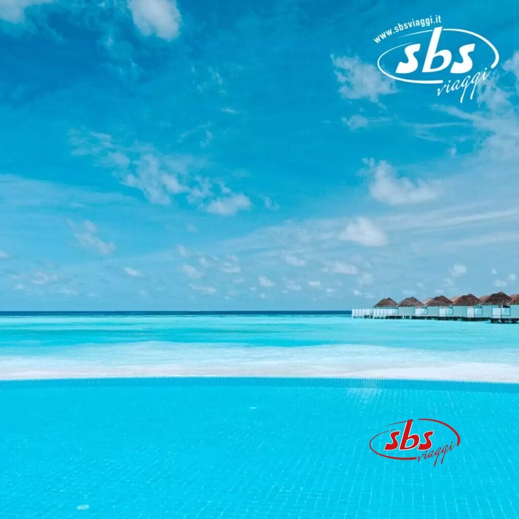 Una piscina a sfioro offre viste mozzafiato sull'oceano sotto un cielo azzurro con nuvole sparse, mentre i bungalow sull'acqua del Nova Maldives Resort punteggiano l'orizzonte, creando uno scenario pittoresco sull'isola di Vakarufalhi.