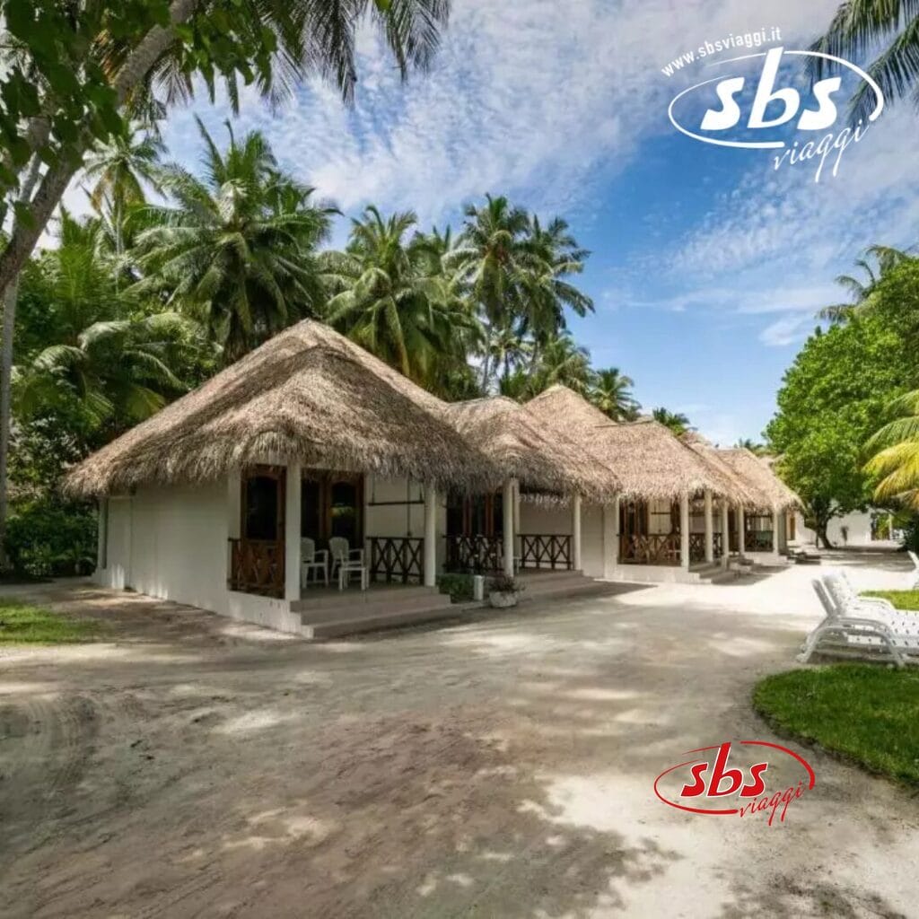 I bungalow con tetto di paglia del Club Coralia offrono portici sereni circondati dalle rigogliose palme e dal verde di Fihalhohi sotto un cielo azzurro con nuvole. Le sedie a sdraio sono graziosamente posizionate lungo il sentiero sabbioso, invitandovi a rilassarvi in paradiso.