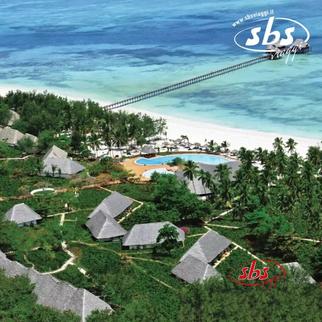 Vista aerea del resort tropicale di Dongwe con ville con tetti di paglia, vegetazione circostante, una piscina, palme e un lungo molo di legno che si estende nel mare turchese.