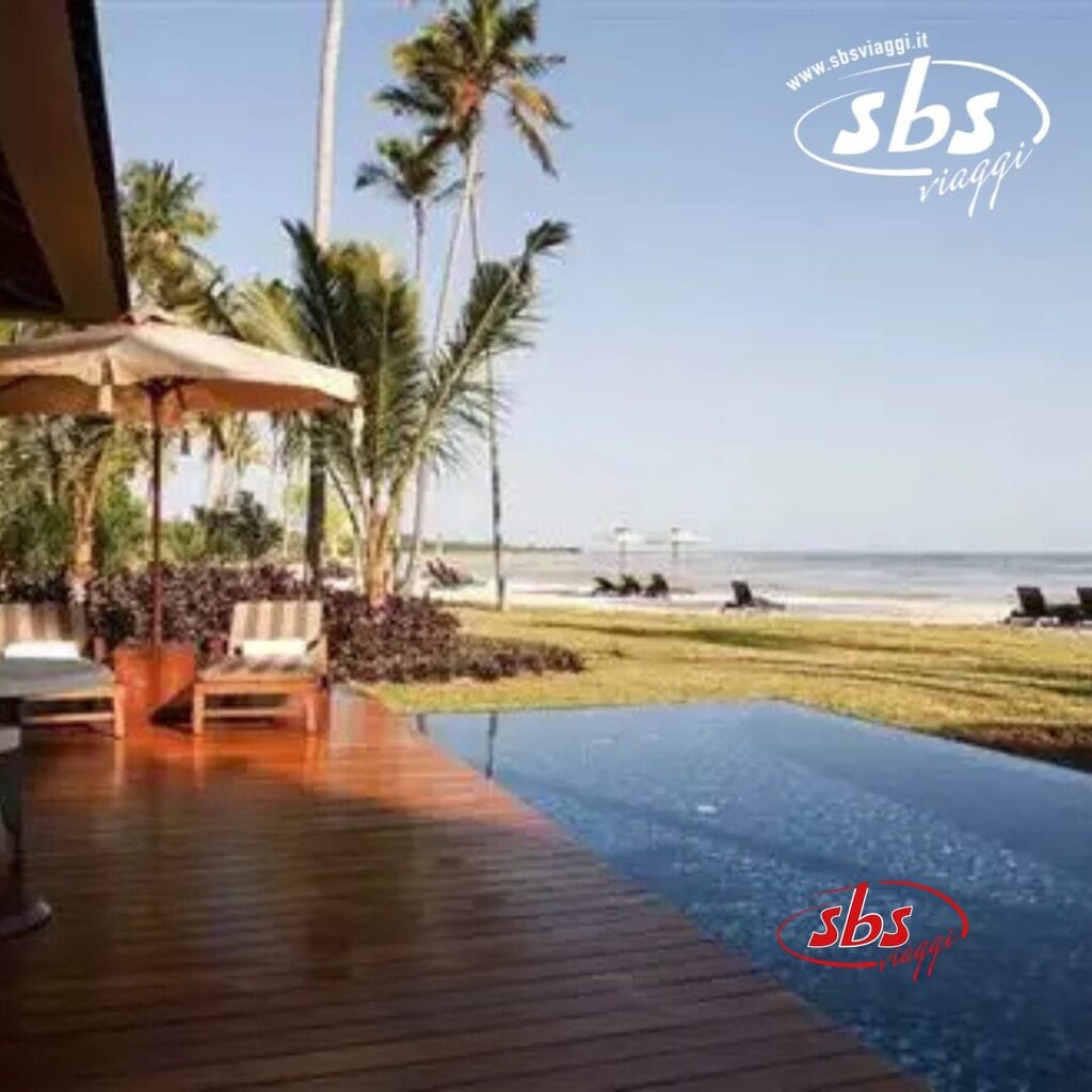 Vista sulla spiaggia tropicale dello Zanzibar Resort, con palme, una terrazza in legno, due sedie a sdraio sotto un ombrellone e una piscina a sfioro.