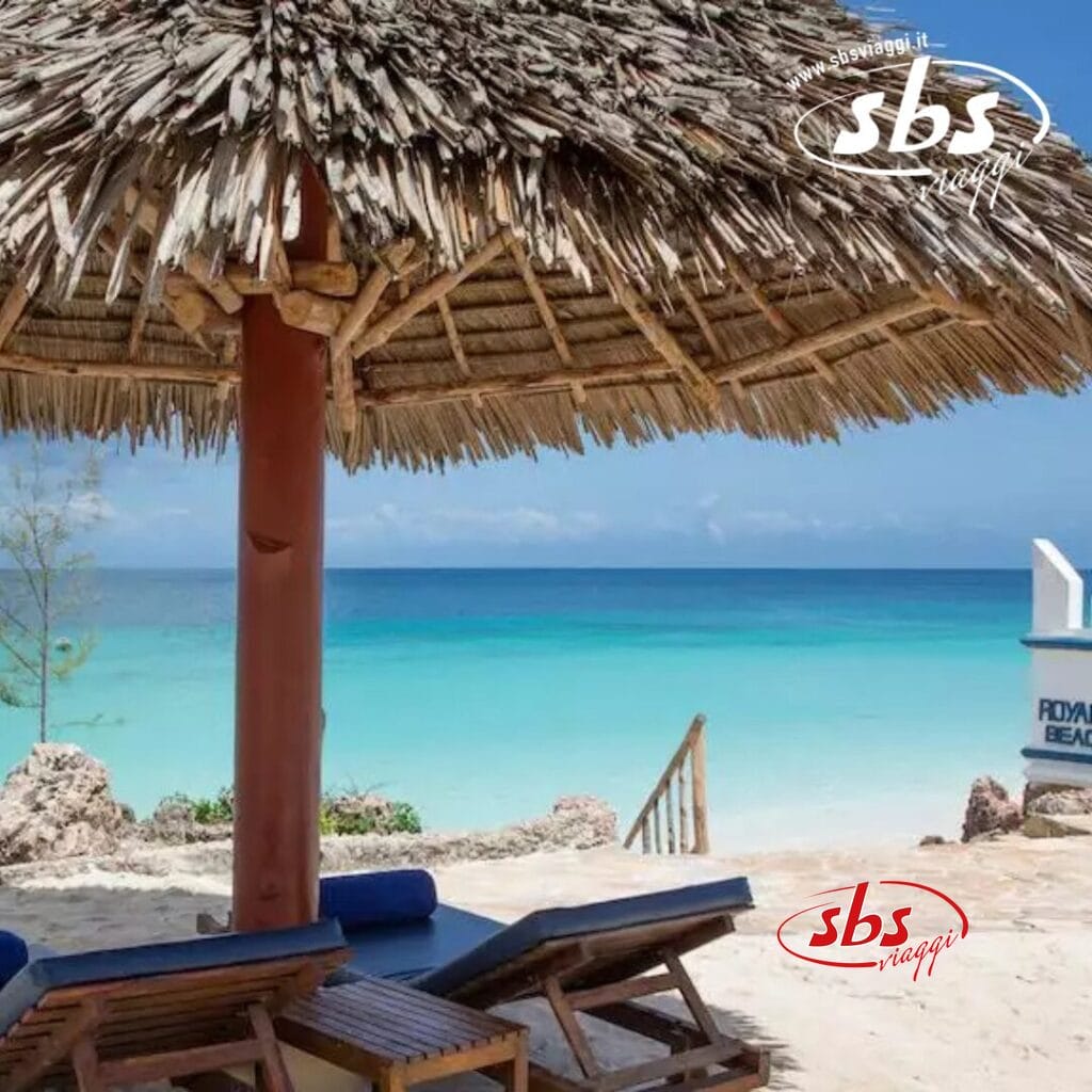 Scena di spiaggia al Royal Zanzibar con un ombrellone di paglia, sedie a sdraio e acqua cristallina sullo sfondo.