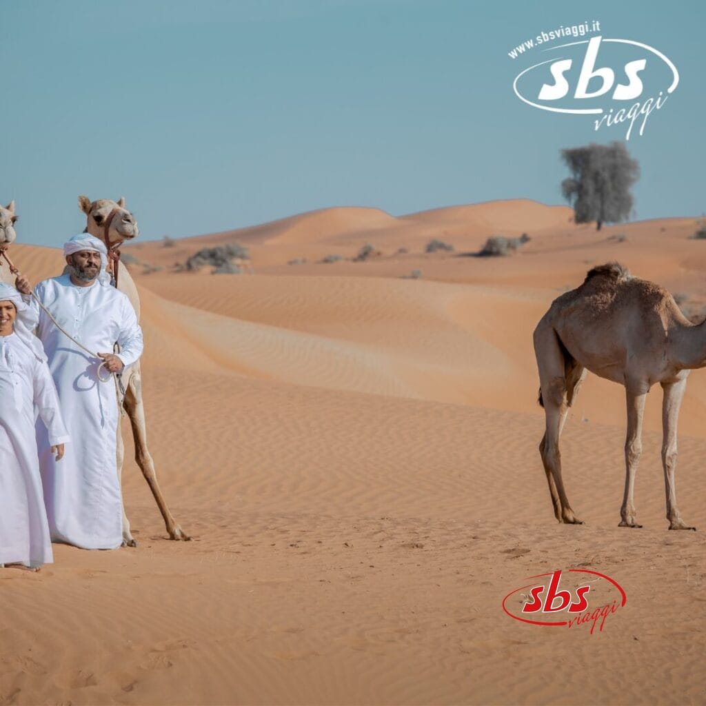 Due abitanti degli Emirati in tuniche bianche sono in piedi accanto a dei cammelli in un incantevole paesaggio desertico, con dune di sabbia ondulate e un cielo limpido.