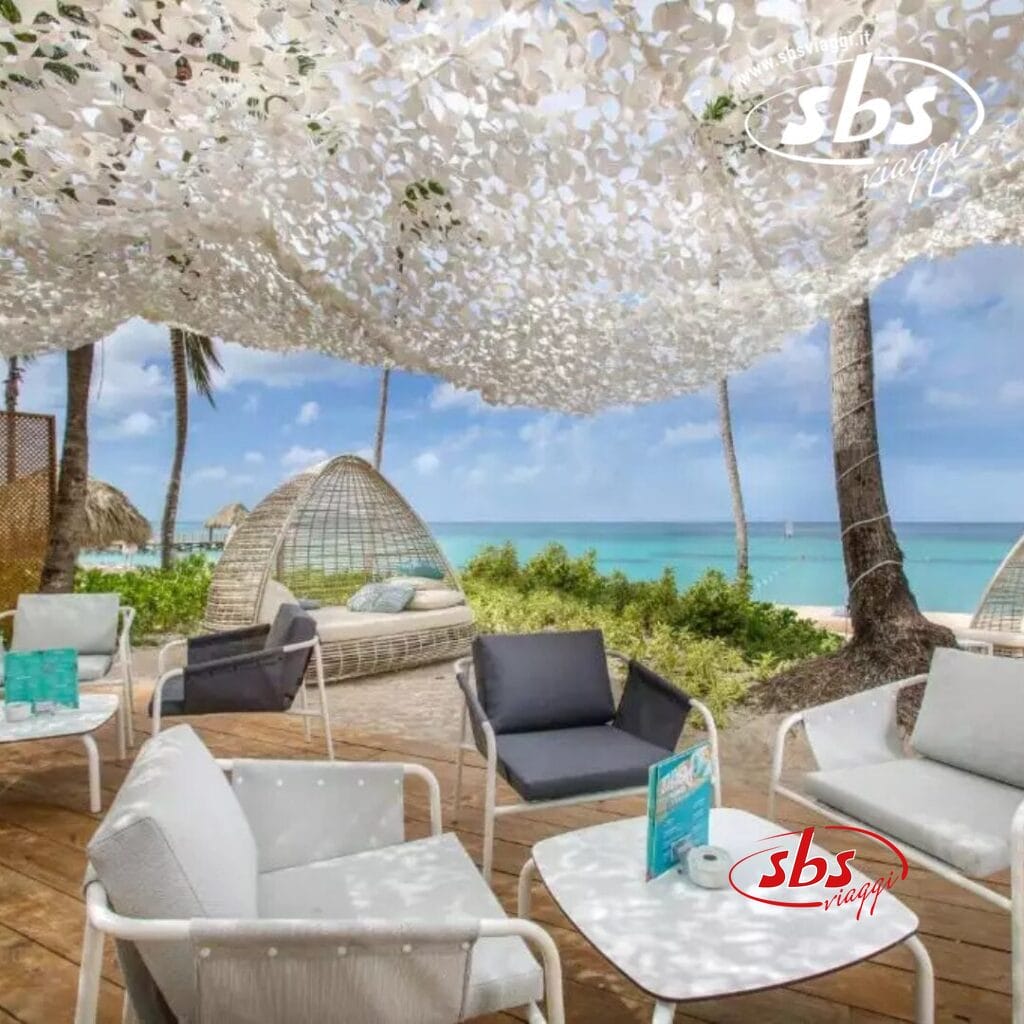 L'area lounge sulla spiaggia del Catalonia Royal La Romana è dotata di sedie in vimini, divani e un baldacchino. Con vista sull'oceano e palme ondeggianti sullo sfondo, questo posto tranquillo è riservato esclusivamente agli ospiti di età superiore ai 18 anni che cercano una fuga tranquilla.