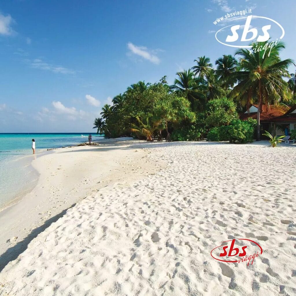 Athuruga Beach offre una vista mozzafiato con le sue rive sabbiose, l'acqua azzurra e cristallina e le palme verdi e rigogliose sotto un cielo parzialmente nuvoloso; una persona si ferma vicino al bordo dell'acqua, forse ammirando la vicina Water Villa in vero stile Seaclub.