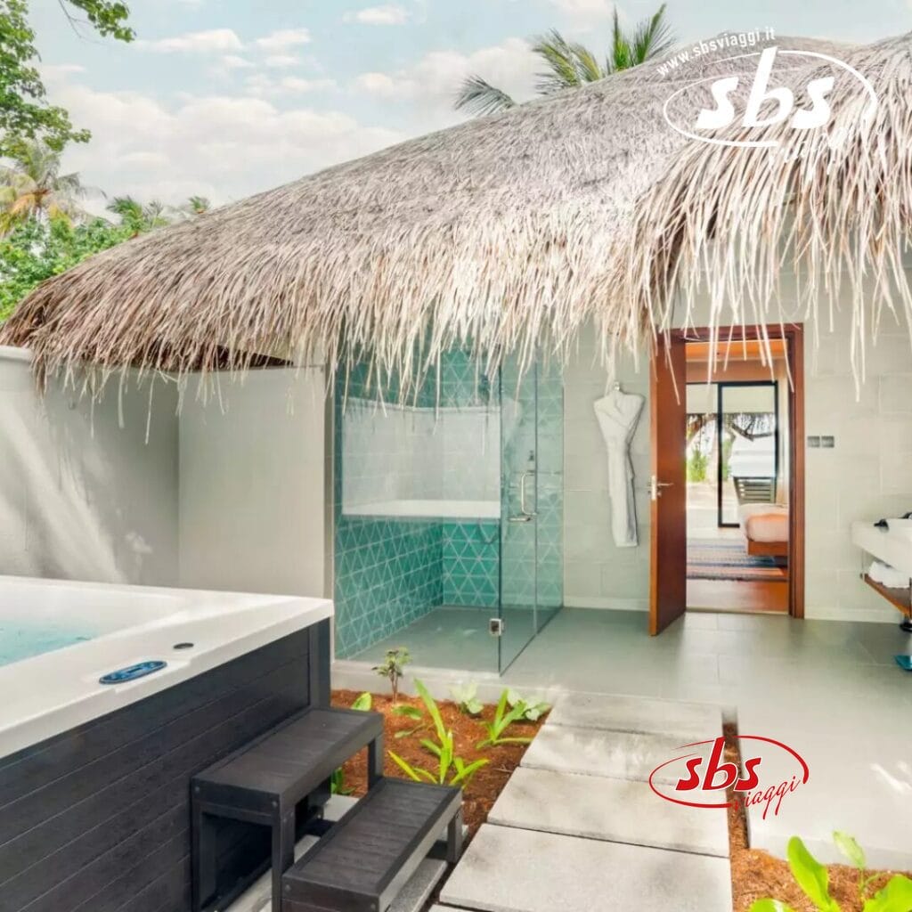 Spa tropicale all'aperto con tetto di paglia, doccia con vetrate e jacuzzi accanto a una porta che conduce all'interno. Concedetevi il relax in questa oasi di Nova Maldives. Un accappatoio è appeso all'ingresso, invitandovi a rilassarvi con stile sull'isola di Vakarufalhi.