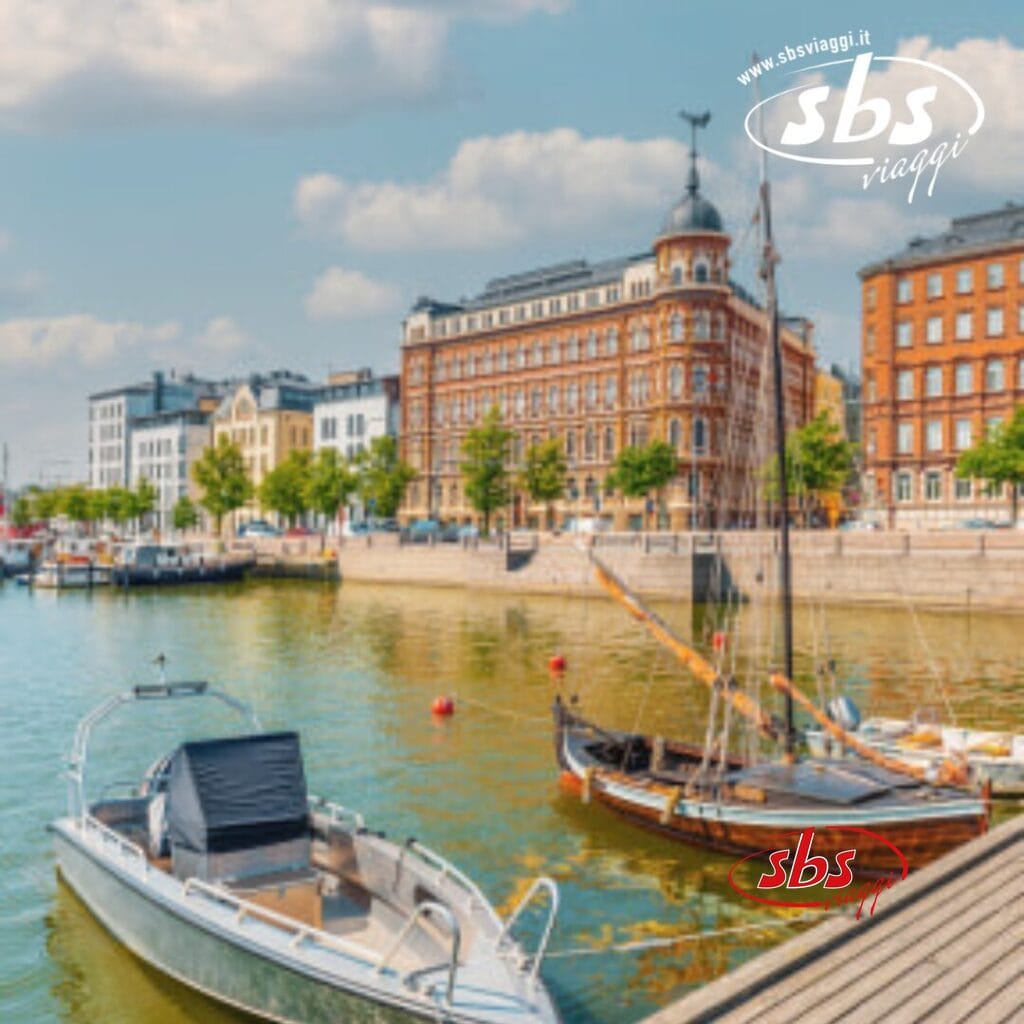 Barche attraccate sul lungomare cittadino con edifici storici sullo sfondo in una giornata di sole, che ricordano il fascino di Helsinki durante una crociera sul Baltico.