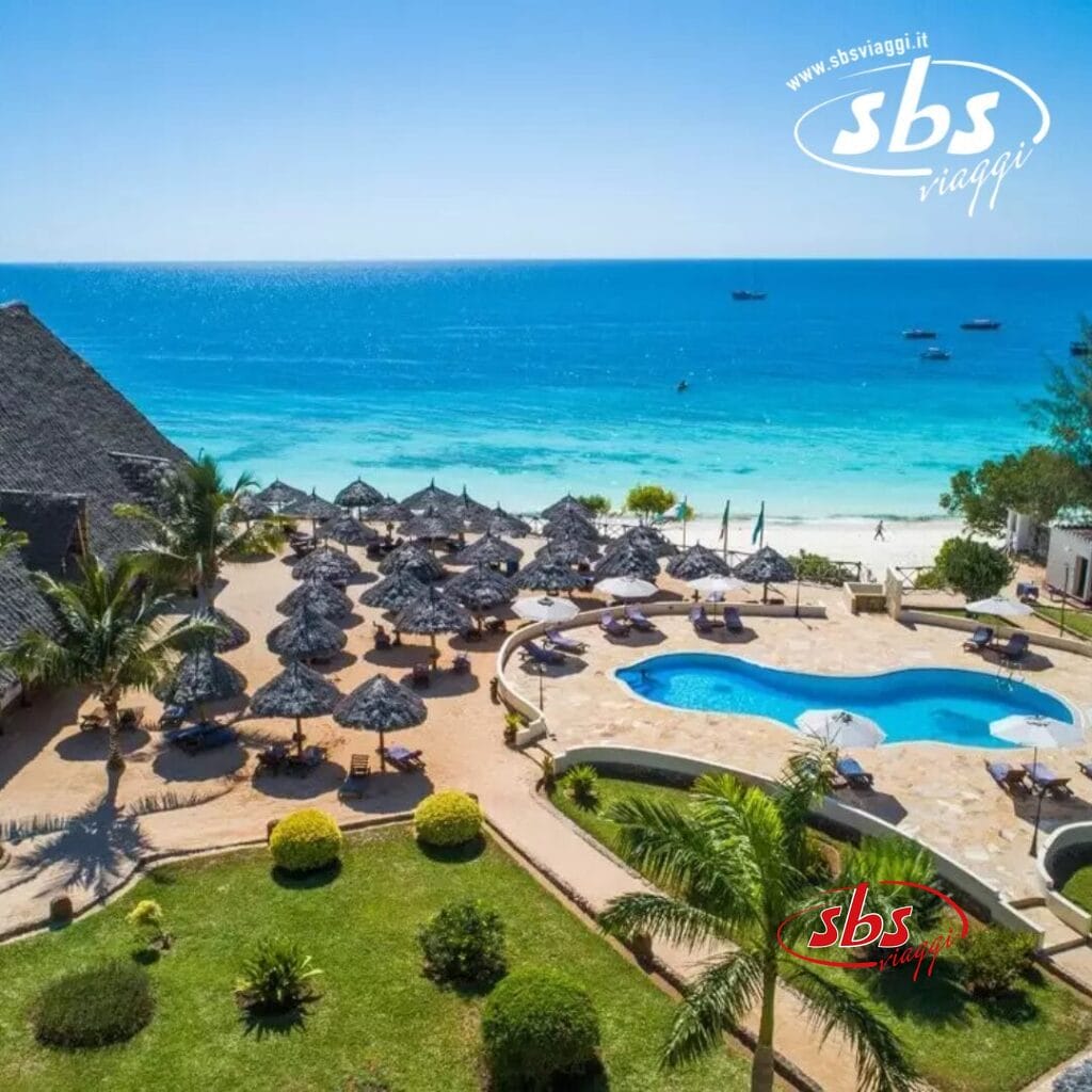 Vista aerea del resort tropicale sulla spiaggia Veraclub con piscina, lettini prendisole e ombrelloni. L'oceano si estende fino all'orizzonte sotto un cielo azzurro e limpido, catturato alla perfezione a Sunset Beach.