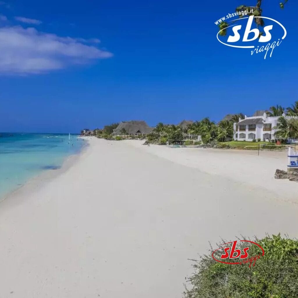 Uno scenario sereno sulla spiaggia del Royal Zanzibar Beach Resort, con sabbia bianca, acqua cristallina, palme ondeggianti e incantevoli edifici sulla spiaggia sotto un cielo perlopiù limpido.