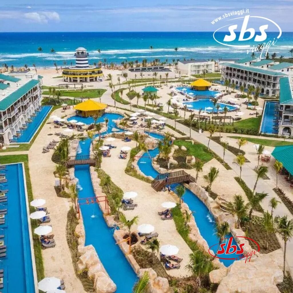 Vista aerea di un resort tropicale con piscine, un fiume lento e sinuoso, lettini e palme. L'oceano è sullo sfondo sotto un cielo azzurro, creando una scena che sembra quasi una bozza automatica, una rilassante boccata di paradiso che cattura senza sforzo l'essenza del relax.