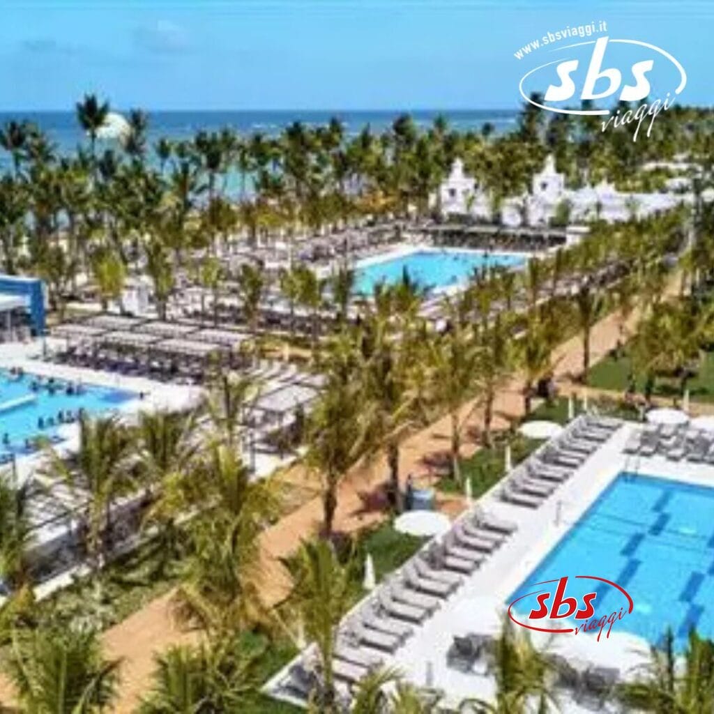 Il resort sulla spiaggia Riu Palace Punta Cana vanta numerose piscine, circondate da palme e sedie a sdraio, con una vista mozzafiato sull'oceano sullo sfondo.