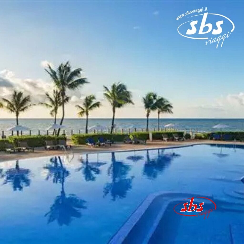 Una piscina serena sulla spiaggia con palme e una vista mozzafiato sull'oceano all'alba, catturando perfettamente la tranquillità. Il logo 