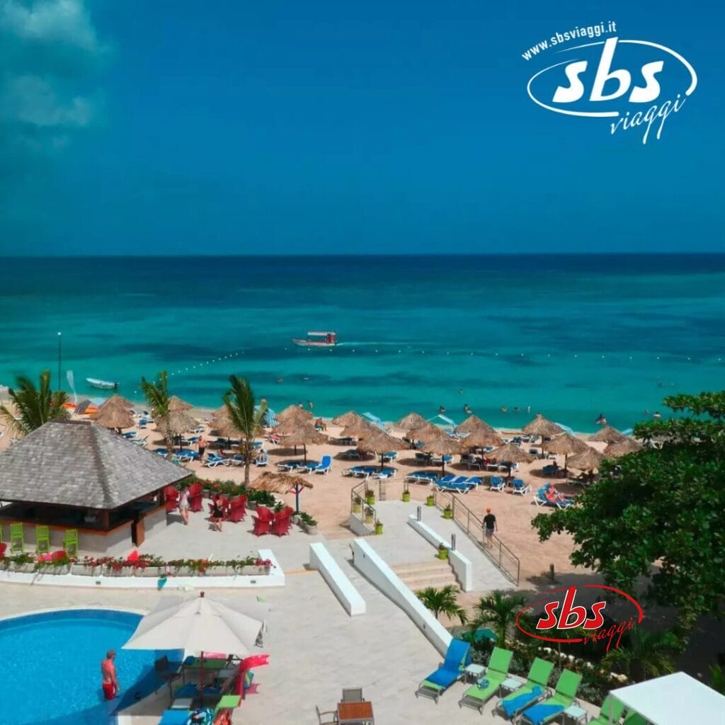 La scena del resort sulla spiaggia Bozza Automatica mostra lettini e ombrelloni a bordo piscina con vista sull'oceano turchese, con i loghi discretamente visibili in alto a destra.