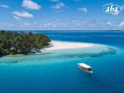 Una piccola barca vicino a un'isola tropicale con sabbia bianca e palme è circondata dall'oceano turchese e blu intenso sotto un cielo azzurro e limpido, catturando la bellezza serena tipica delle Maldive, che ricorda il Club Coralia Fihalhohi.