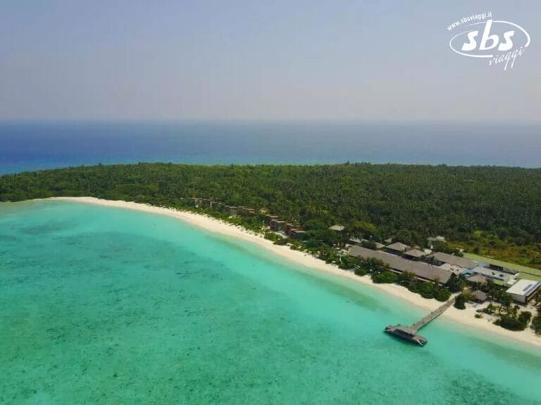 Vista aerea di un'isola tropicale con vegetazione lussureggiante, una lunga spiaggia sabbiosa perfetta per passeggiate a piedi nudi e acqua turchese, con un molo che si estende dalla riva vicino a un eco-hotel.