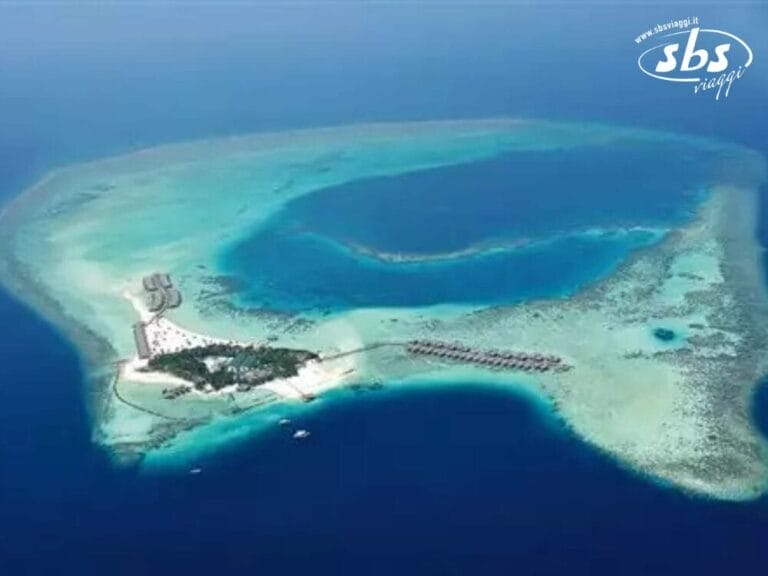 Vista aerea di un'isola tropicale delle Maldive, circondata da un oceano azzurro e limpido, caratterizzata da spiagge sabbiose e bungalow sull'acqua che si estendono dalla riva, che ricordano il pittoresco paradiso del Constance Moofushi.